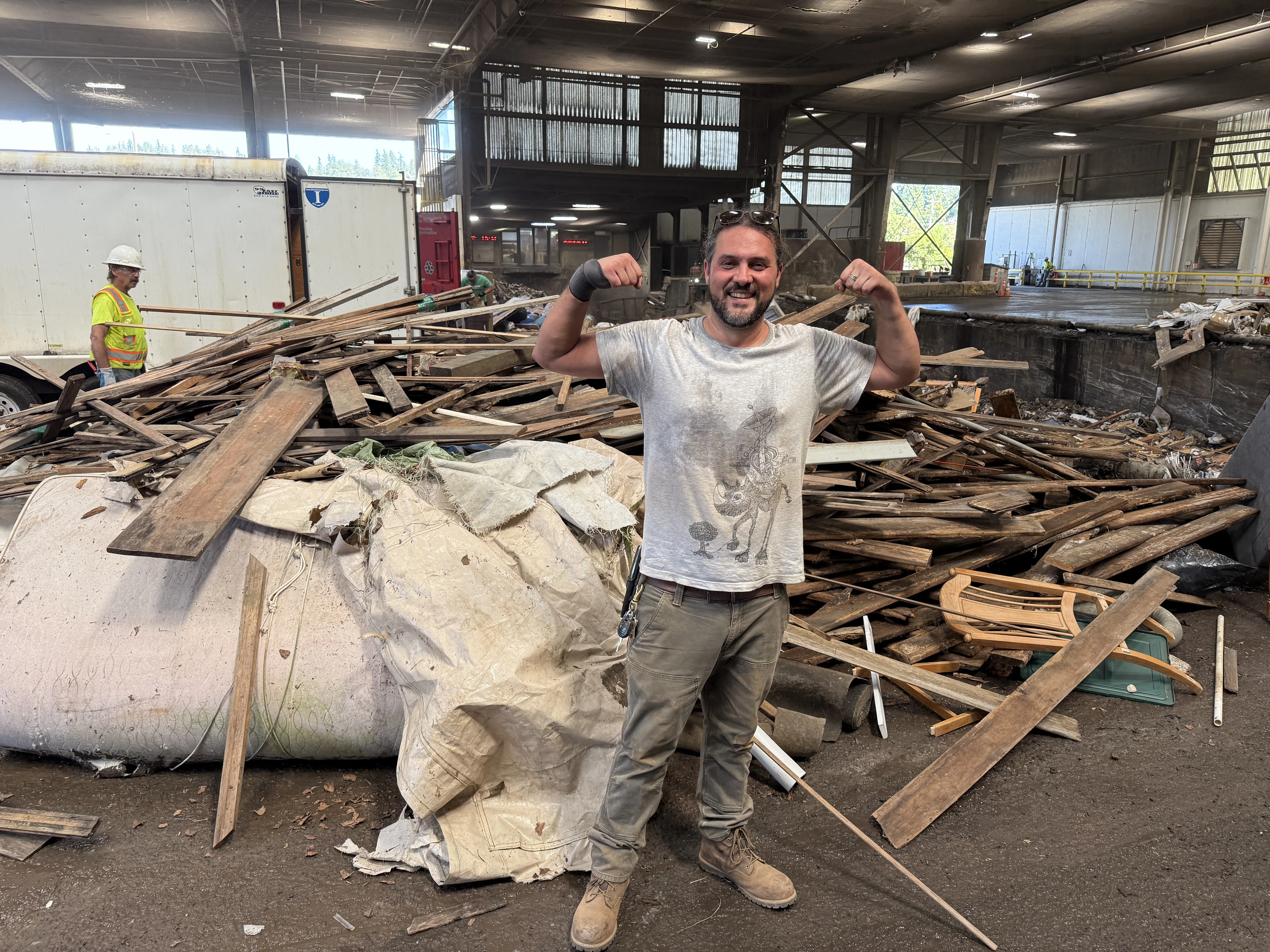 Odyssey Hauling team member standing in front of reclaimed wood and debris